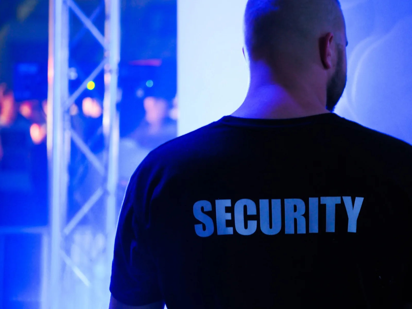 A door supervisor in a SECURITY shirt watching a venue floor