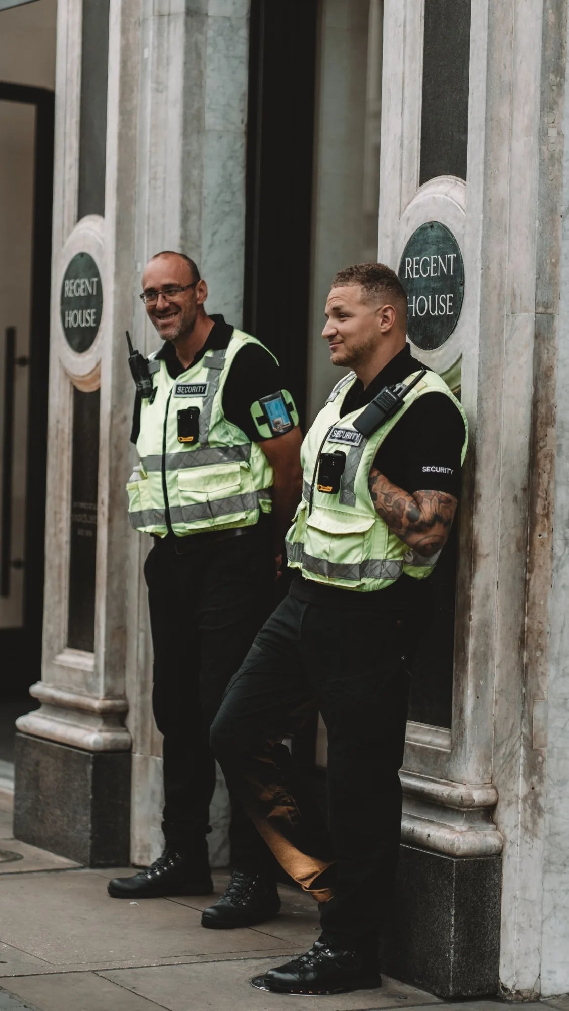 Two security officers in hi-vis vests outside a UK office building
